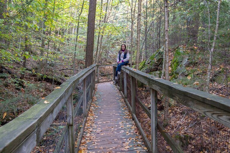Woman sat on fence of boardwalk through forest