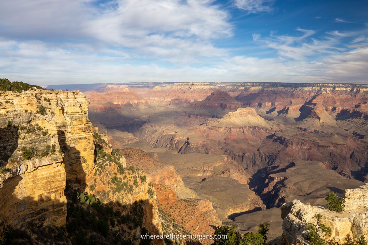 Photo of Mather Point in Grand Canyon South Rim at sunrise with deep canyon walls lighting up, yellow colors inside the canyon and light clouds above