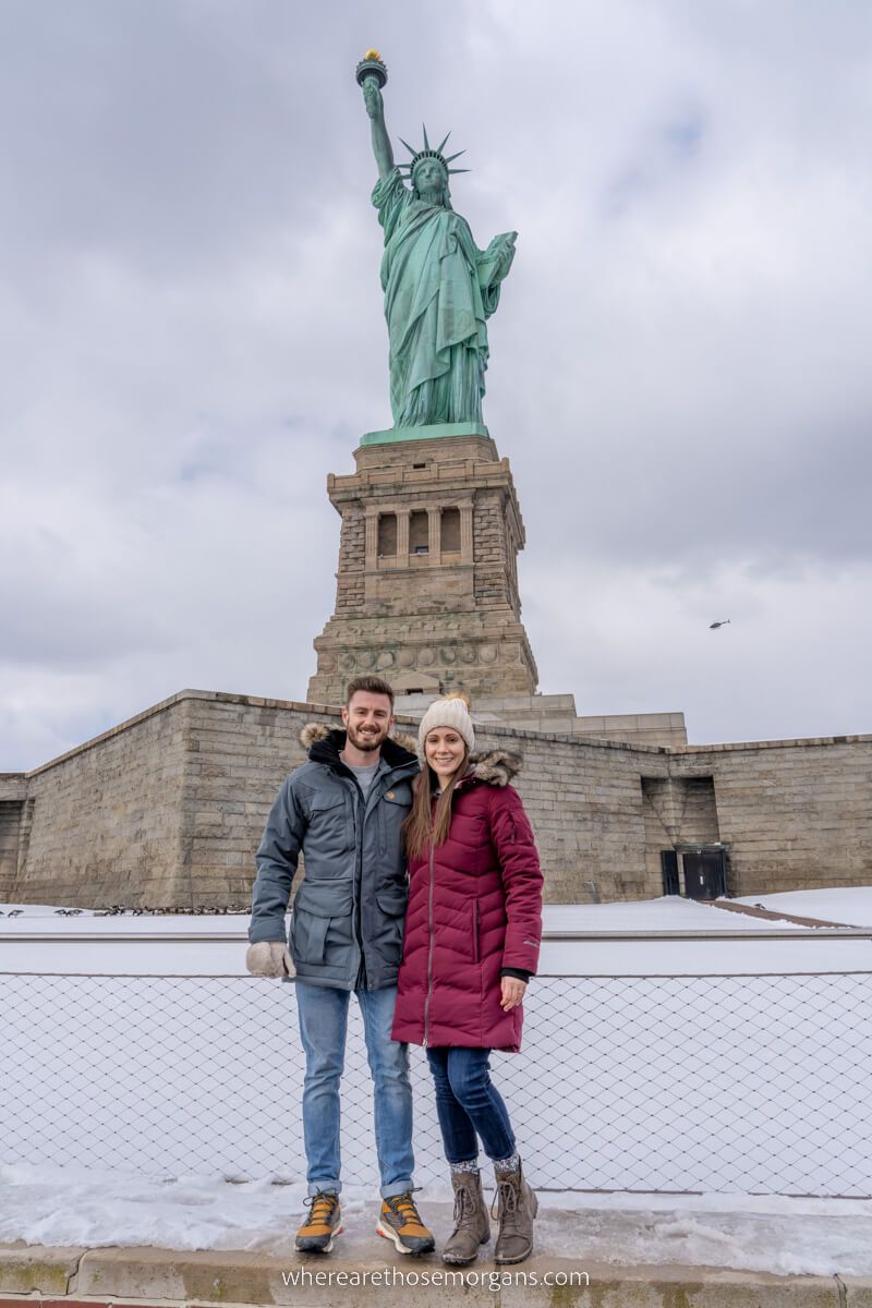 Couple standing in front of Statue of Liberty on Liberty Island with snow on the ground