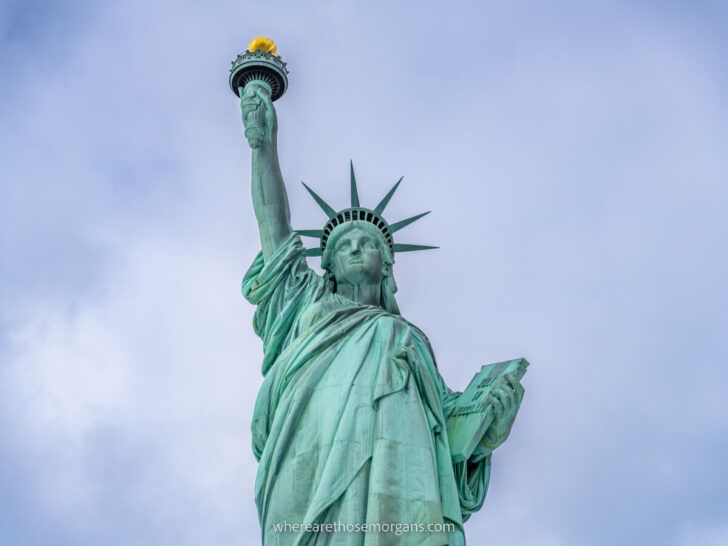 The Statue of Liberty close up holding torch aloft into a cloudy sky from the Statue Cruises ferry in NYC