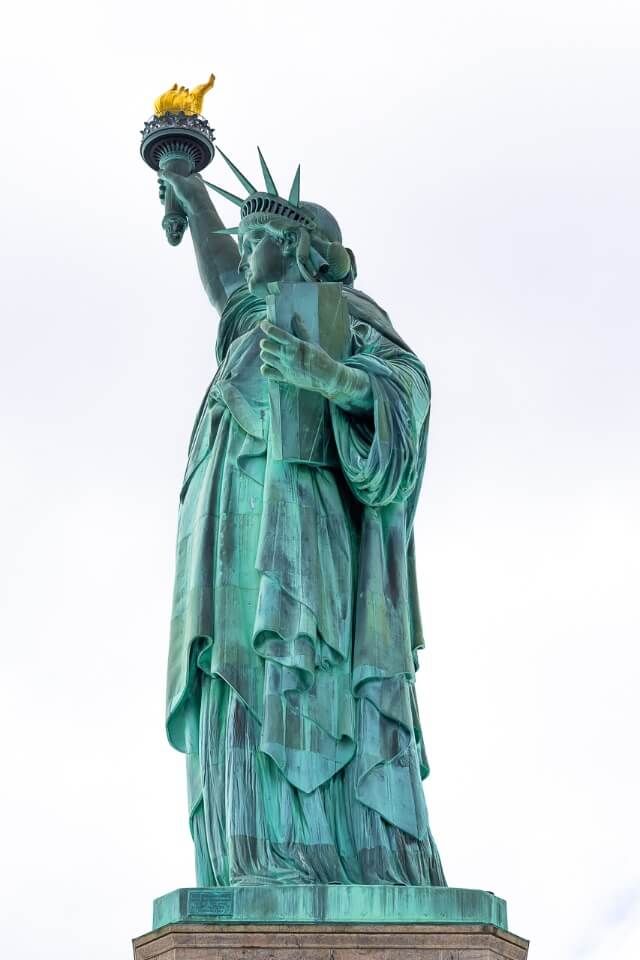 Amazing photograph of statue of liberty taken from close up and to the side with a grey sky accentuating its green color