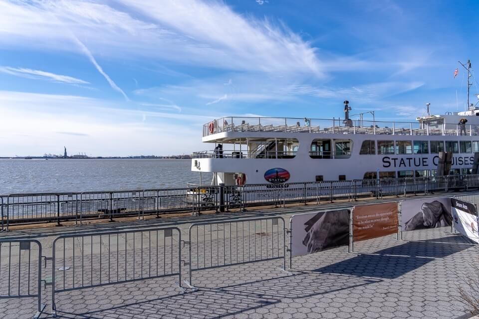 Statue Cruises ferry at the dock with statue of liberty far off in the distance