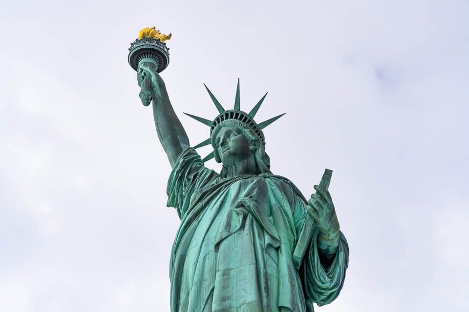 Statue of Liberty on liberty island is one of the best things to do in lower manhattan new york city itinerary green statue and yellows torch in grey clouds