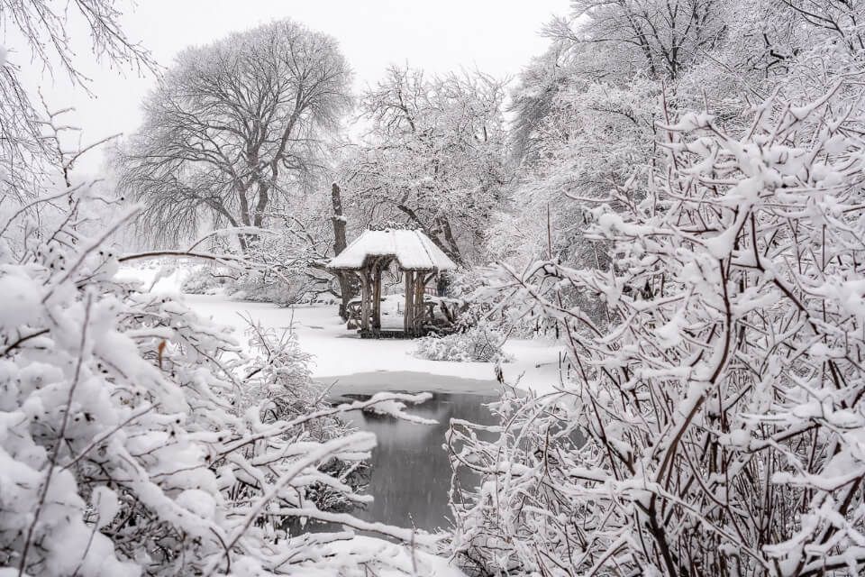 Wagner Cove wooden shelter on a winter snow day in central park from a viewpoint over frozen lake