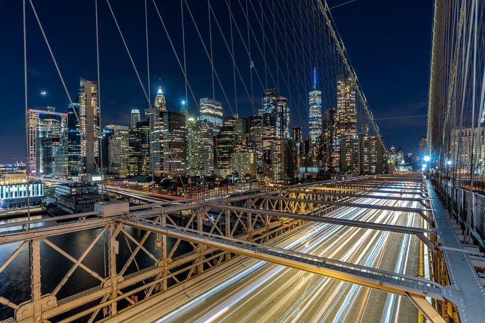 Lower Manhattan illuminating at night with long exposure creating light effect on Brooklyn Bridge one of the very best NYC photography locations of all