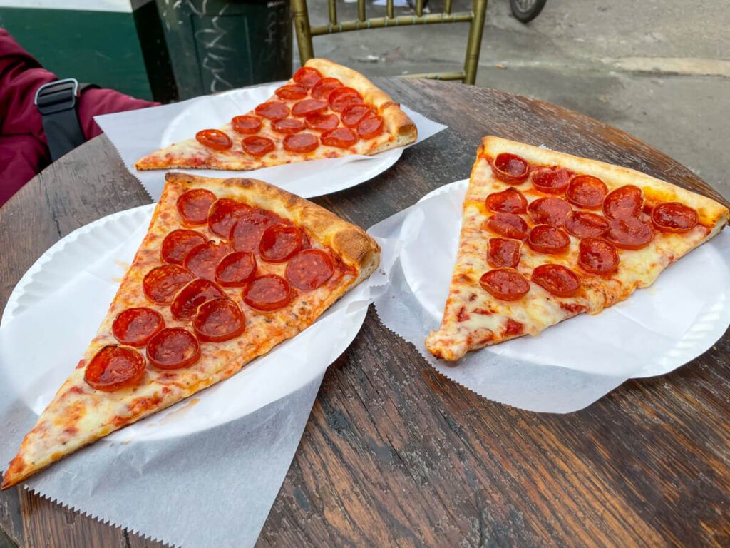 three slices of classic new york pizza with pepperoni on paper plates