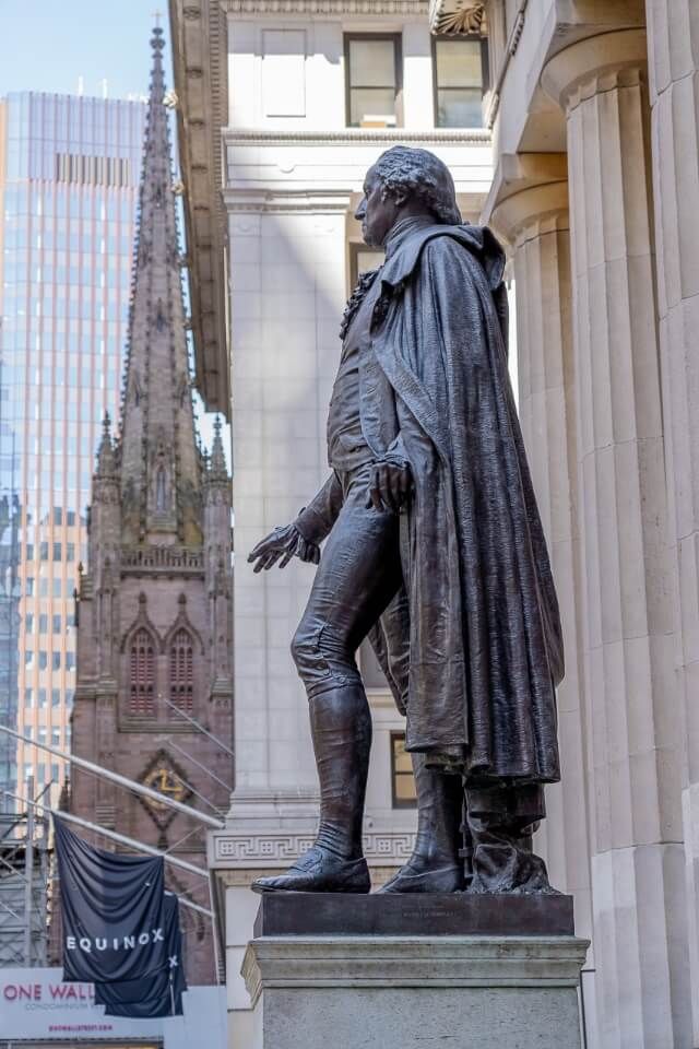 George Washington statue at federal hall on wall street and trinity church in background one of the best places to visit on a first trip to new york city