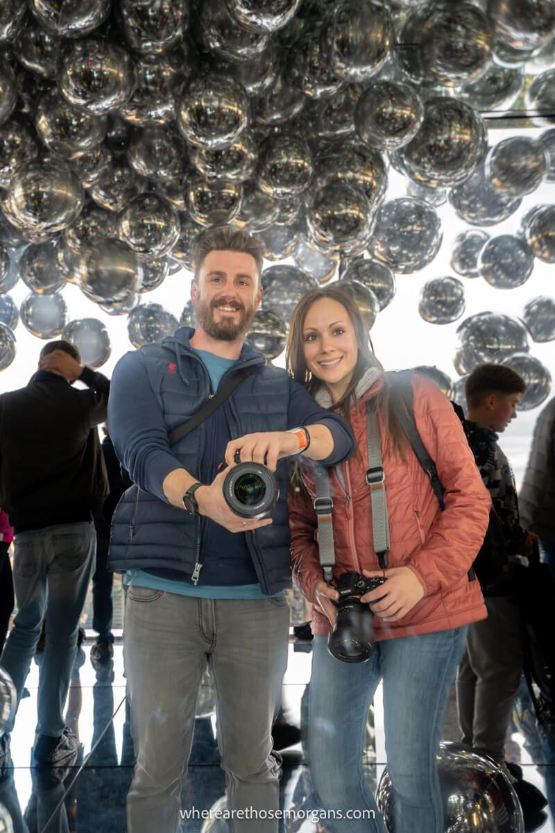 A couple taking a photo of themselves reflecting in mirrors at summit one in New York City with silver balloons on the ceiling