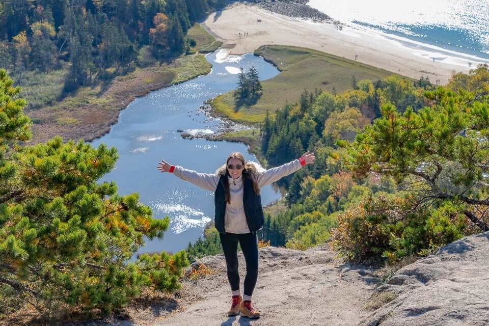 Woman at the summit of a hike in maine with beach behind