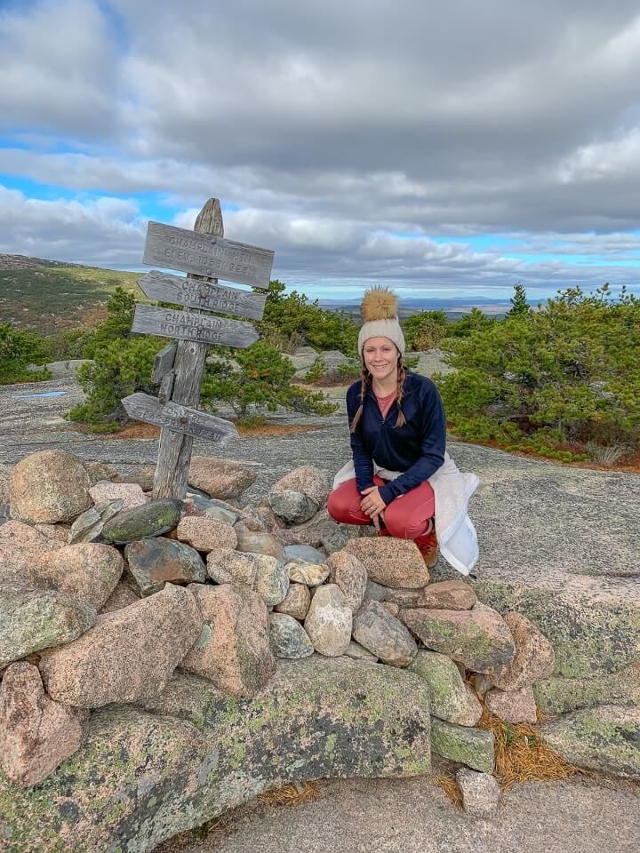 Woman at the champlain mountain summit sign after hiking the precipice trail in acadia