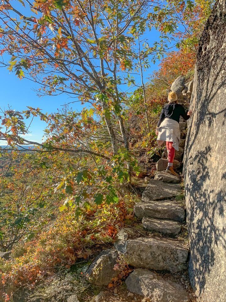 Woman climbing a narrow set of stairs surrounded by colorful leaves on precipice trail hike in acadia national park maine