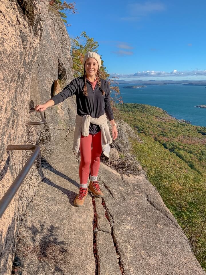 Woman standing on narrow granite rock with steep drop off to side