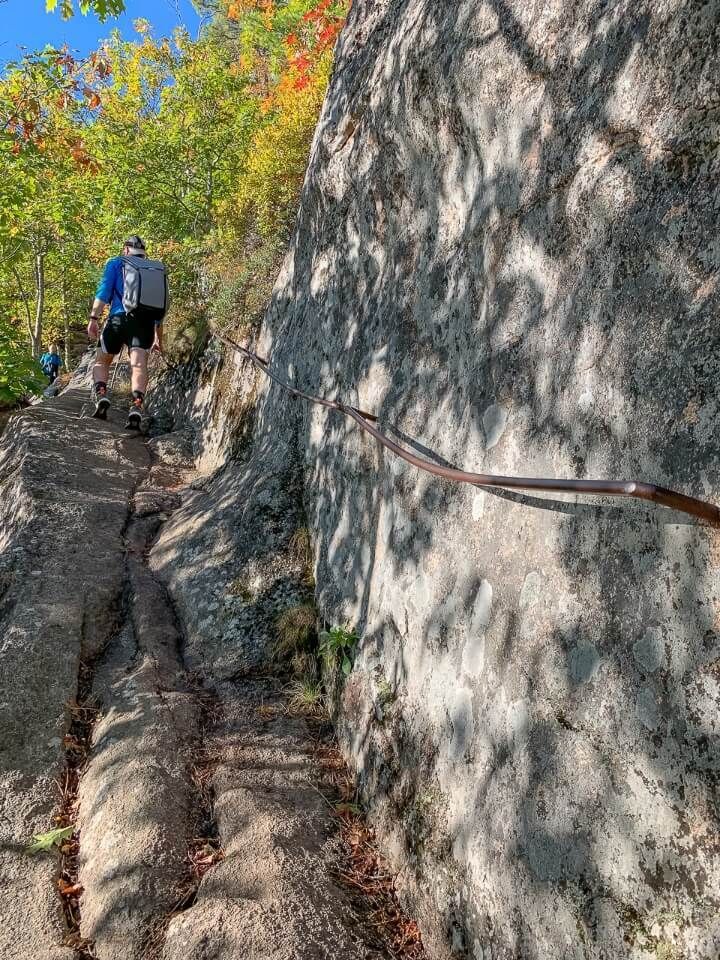 Man climbing steep rock using iron rail for assistance
