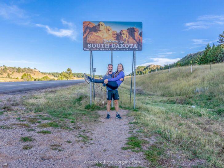 Mark and Kristen from Where Are Those Morgans underneath the South Dakota welcome sign staying at the best places and hotels near Mount Rushmore in the Black Hills
