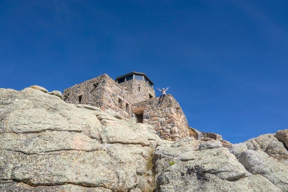 Black Elk Peak trail summit fire watchtower with woman arms stretched out blue sky