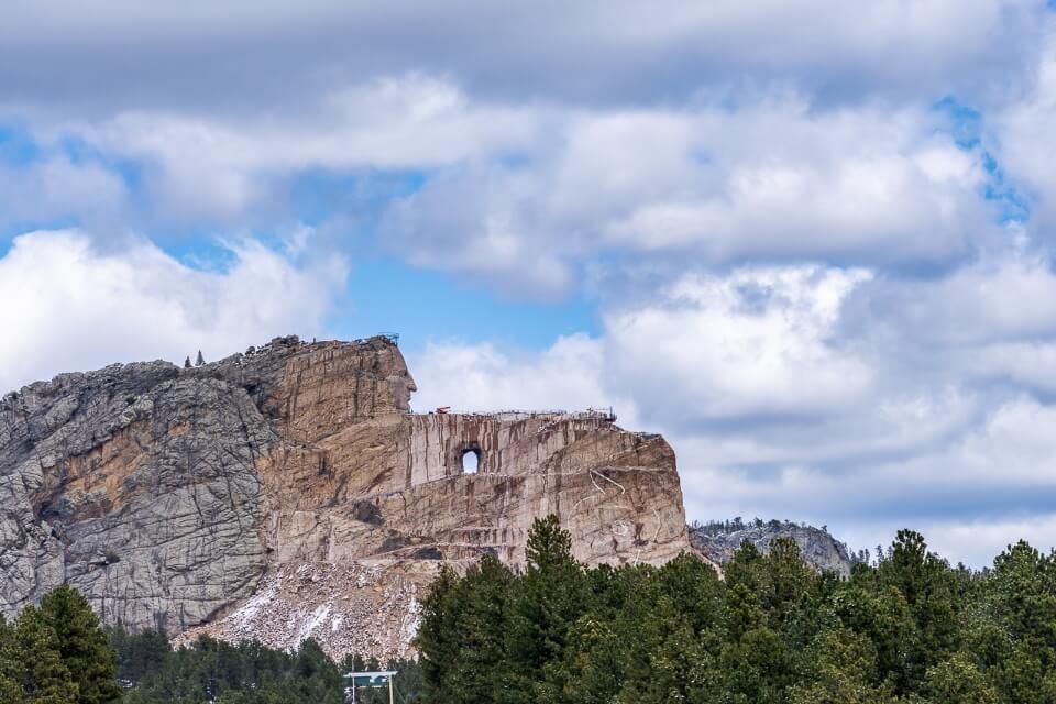 Crazy horse sculpture is a popular place to visit near mount Rushmore taken from afar with trees and puffy clouds