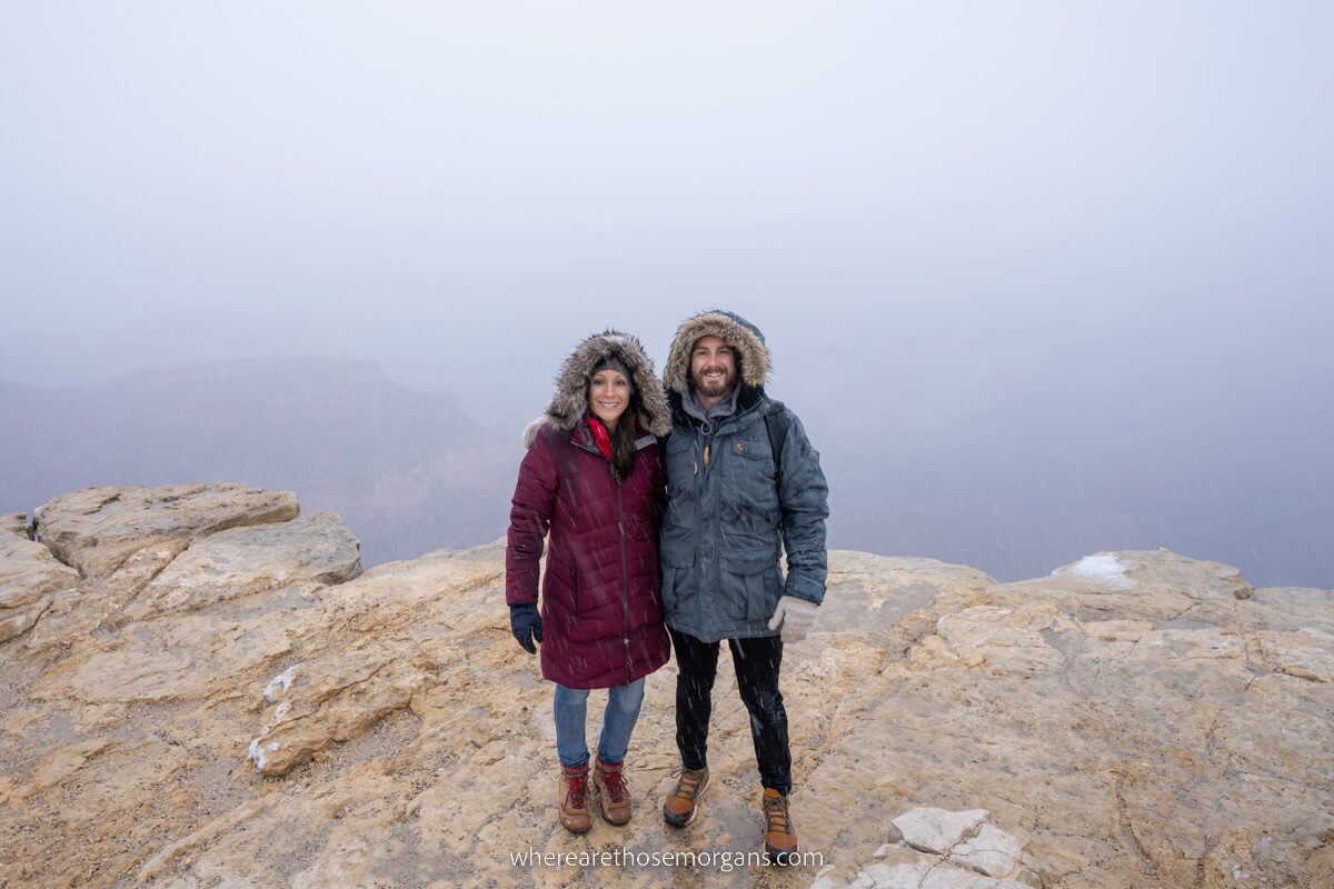 Couple wearing heavy winter coats on a foggy day standing on rocks