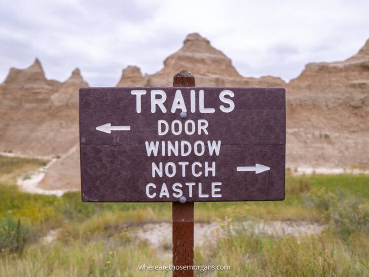 Brown sign showing Badlands National Park hiking trails with directions to the trailheads and colorful rock formations in the background
