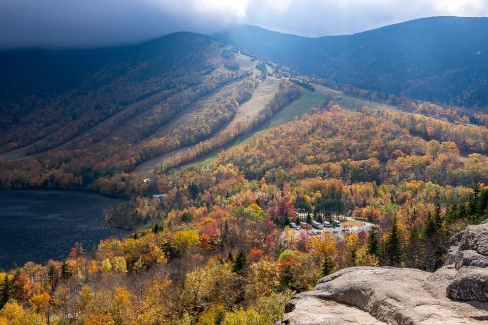 Vibrant Fall foliage colors from the summit of Artists Bluff Trail in NH with sun rays and dark clouds