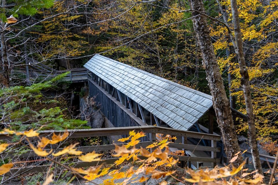 Sentinel Pine Covered Bridge in Flume Gorge Franconia Notch State Park New Hampshire is one of the prettiest wooden bridge in New England with Fall colors surrounding and crossing the Pemigewasset River