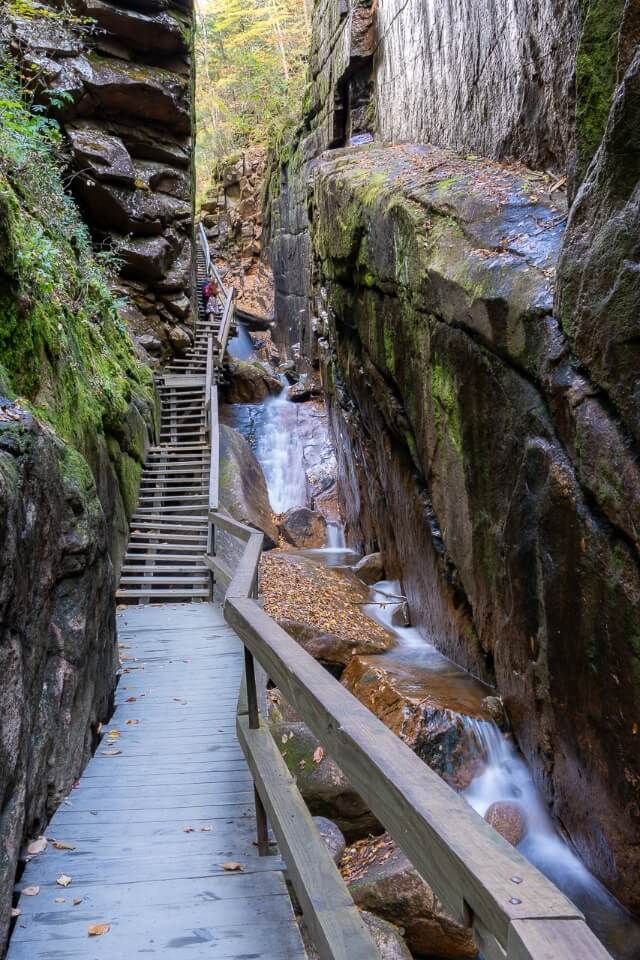 Narrow boardwalk and steps hugging granite walls with light waterfalls flowing in flume gorge franconia notch NH