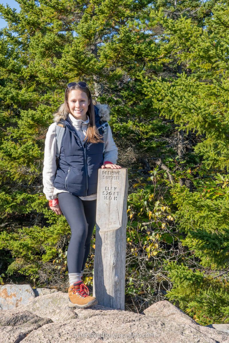 Hiker standing next to the Beehive Trail summit marker on a sunny day in Acadia during October