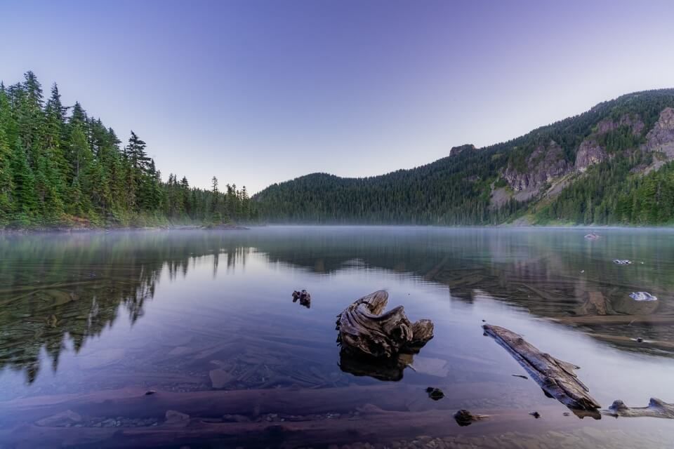 Purple sky at dawn sunrise Mowich Lake wonderland trail beginning of Tolmie Peak trail in Mt Rainier national park still flat water thin layer of fog