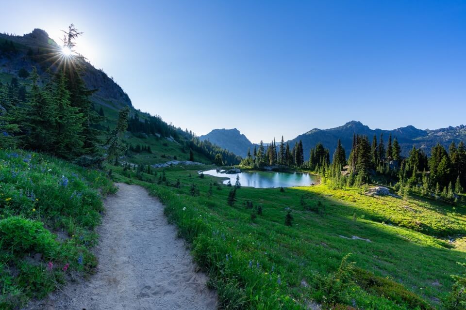 naches peak loop is one of the best short hikes in mount rainier starburst with the sun overlooking a lake with dusty trail at dusk in Washington