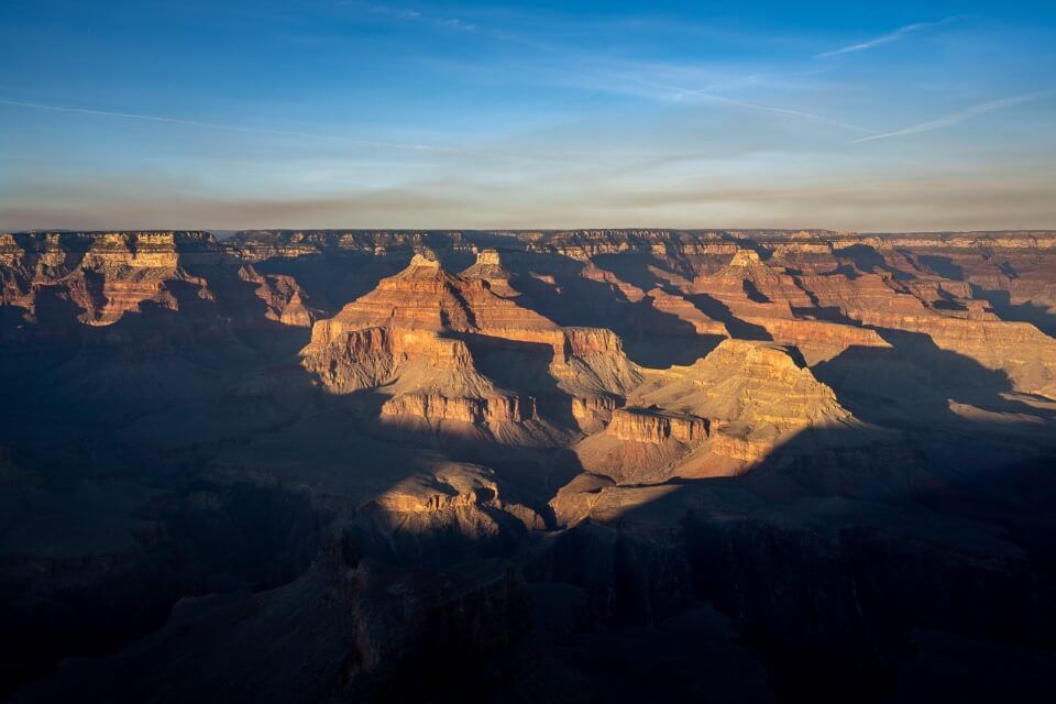 Extreme shadows cast in grand canyon national park south rim moments before dusk with bright yellow light illuminating Powell Point views