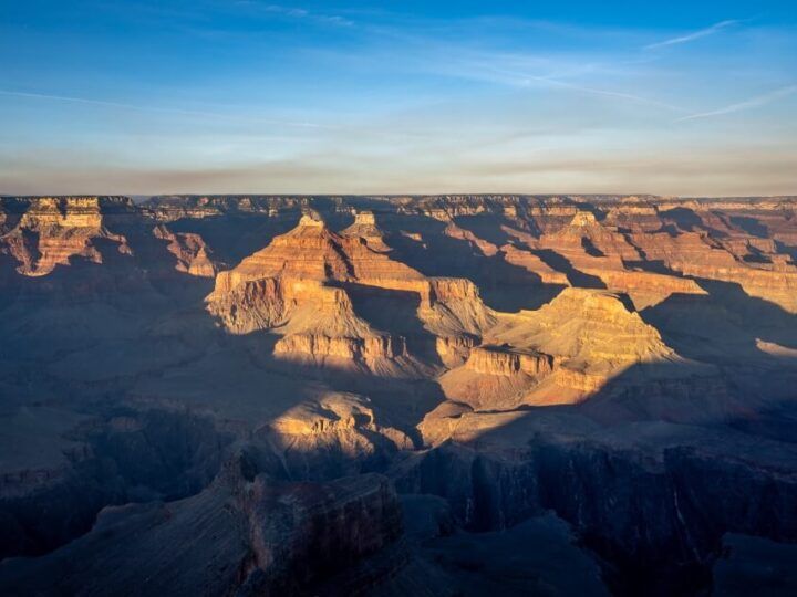 Grand Canyon national park glowing under sunlight with canyon in shadow and blue sky perfect weather and best time to visit