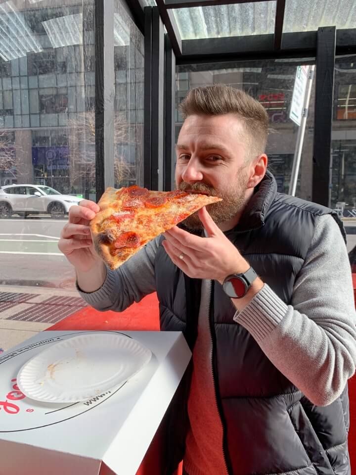 Mark eating a large pepperoni pizza slice in Manhattan