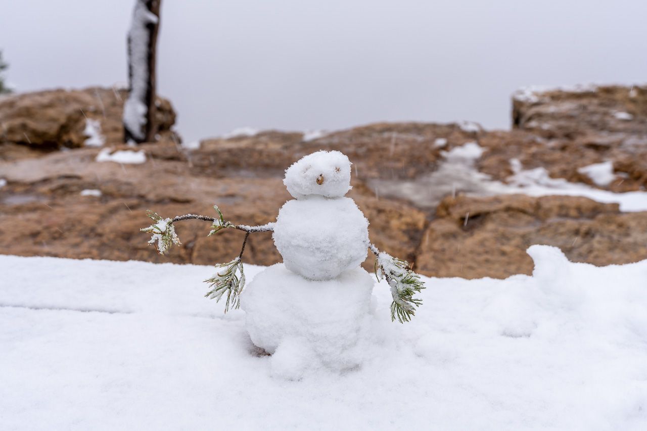 A small snowman with twigs for arms and stones for a face sat on snowy rocks at Grand Canyon South Rim in the winter