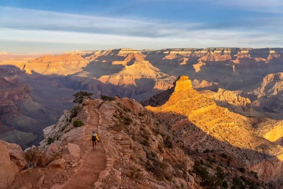 Bright yellow sunrise making the grand canyon glow with a hiker walking down South Kaibab trail