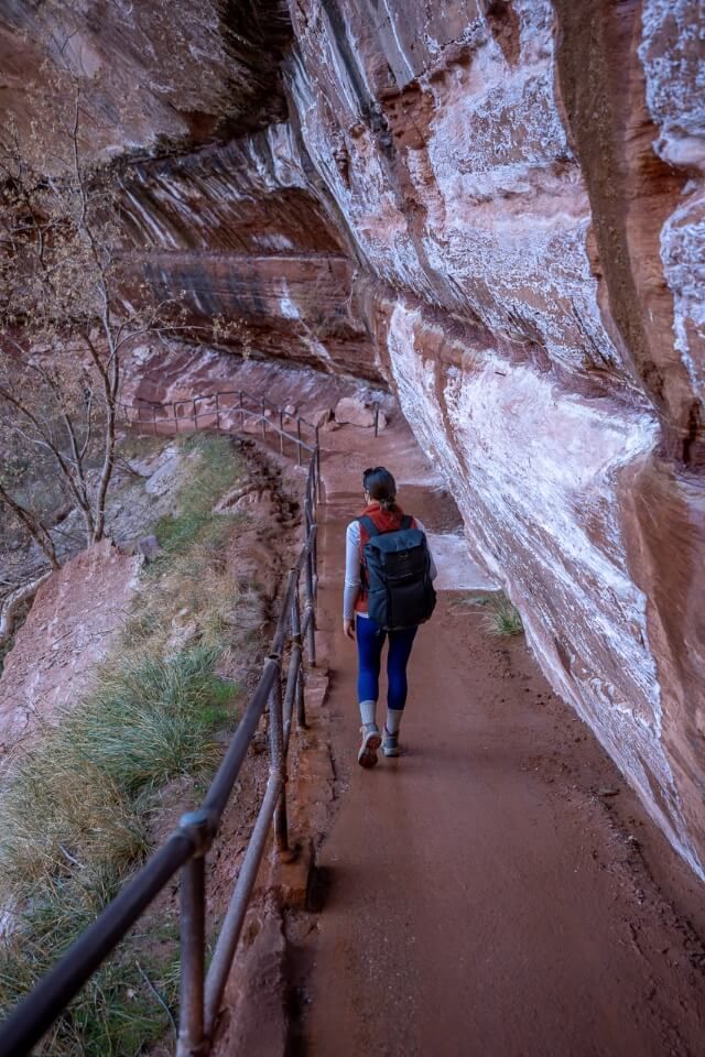 walking on a narrow path with barrier underneath overhanging rocks with wet floor