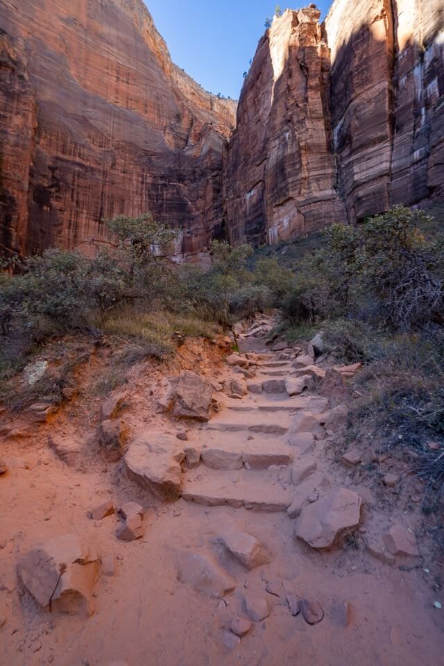 Dirt and sand hiking path leading up toward huge canyon walls in utah