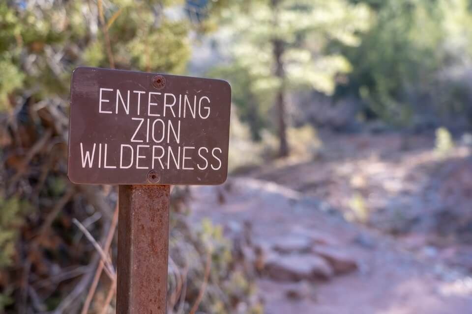 Sign showing entering wilderness of national park in utah with hiking path behind