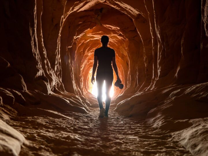 Photographer hiking belly of the dragon in kanab utah silhouette against light at the end of the tunnel