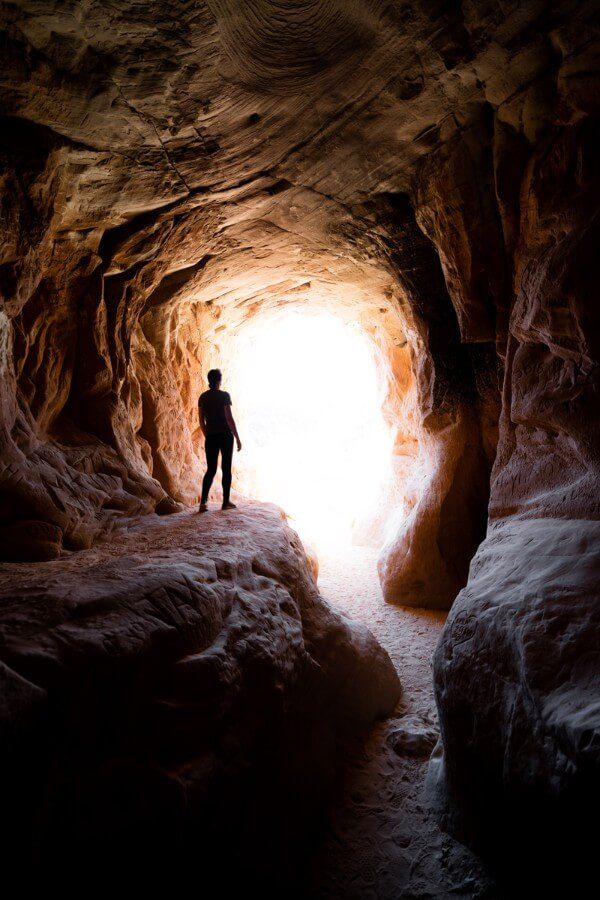 Silhouette of woman hiking through belly of the dragon tunnel in kanab utah with light beaming inside