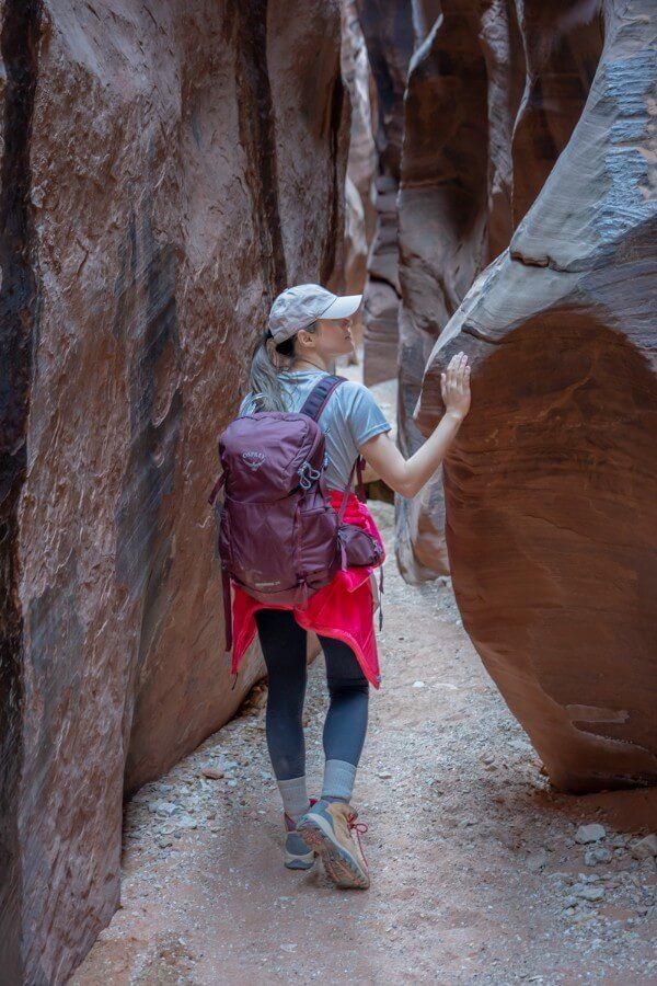 Hiker walking through narrow walls of buckskin gulch slot canyon from wire pass trailhead touching a rock
