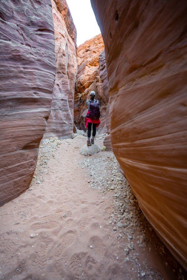Hiker in distance walking on sandy trail flanked by two orange walls of rock