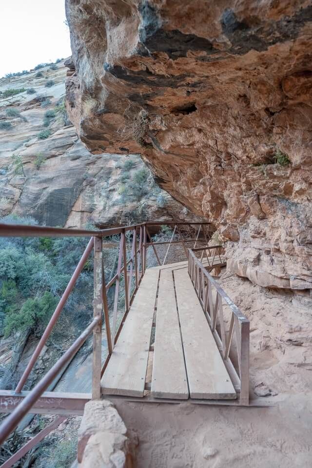 Wooden bridge with metal barrier hugging a canyon wall