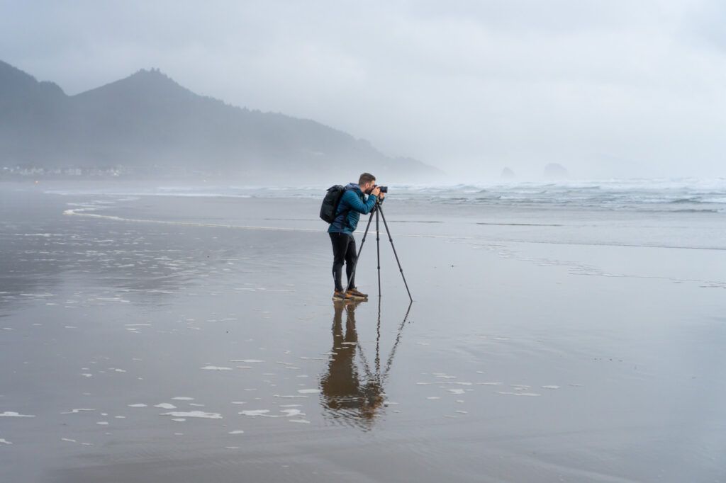 Man taking a photo on Cannon beach of the waves crashing into the beach