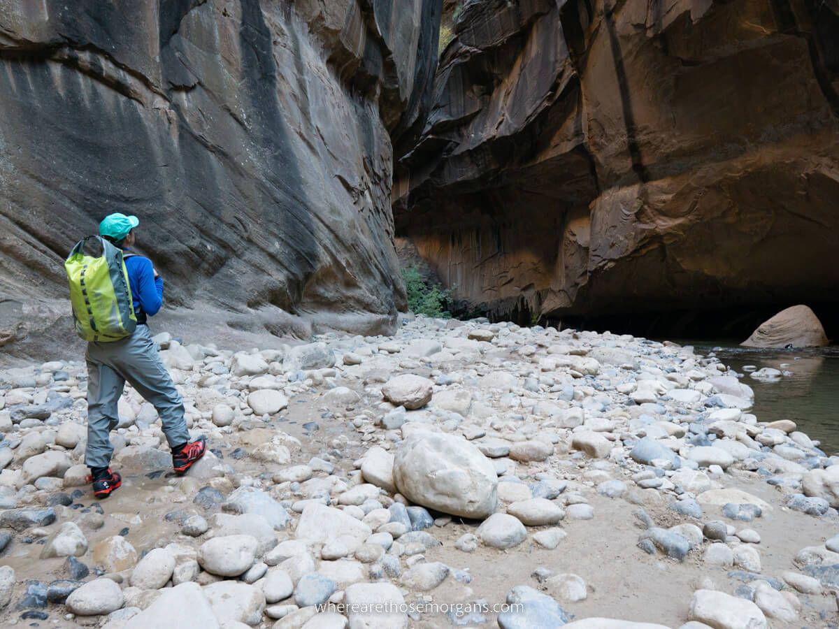 Hiker in waterproof clothing walking a rocky trail inside a slot canyon in Zion