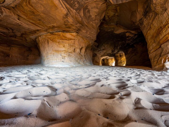 Deep sand dunes surrounded by natural caves formed in sandstone rock at Moqui Caverns near Kanab Utah light penetrating and illuminating orange walls