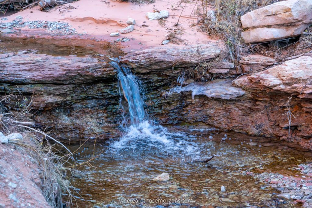 Small waterfall plunging into a pool from orange rocks