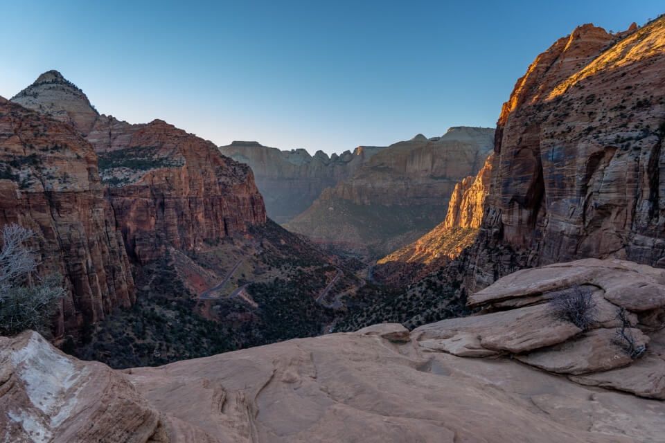 Canyon Overlook at sunset with road zig zagging down into a valley and towering orange walls to either side