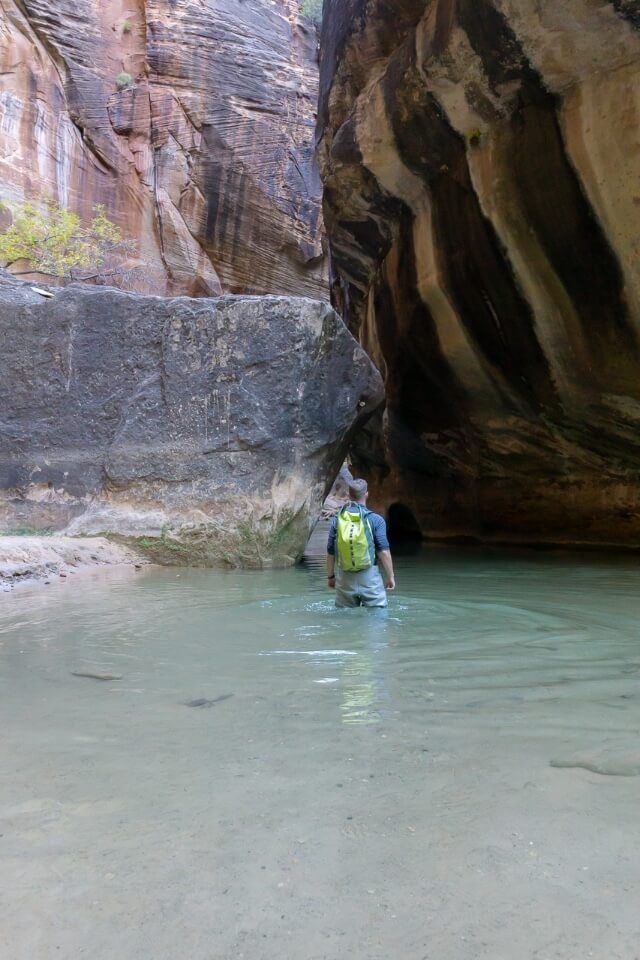 Hiking The Narrows in Zion National Park in Winter dry pants package with waterproof backpack waist deep in water through a narrow slot canyon