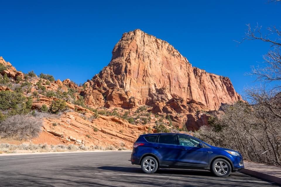 Car parked in a parking lot with orange canyon walls behind on a sunny day with blue sky