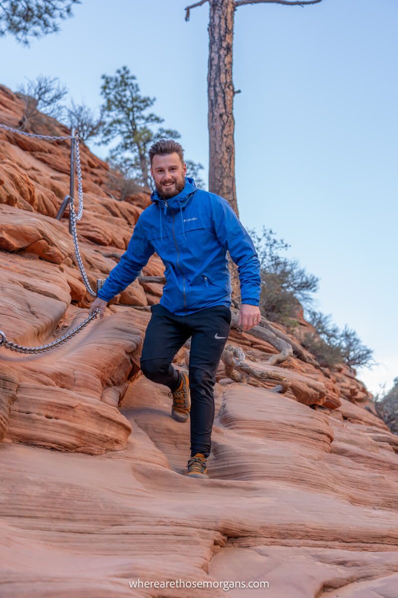 Hiker in blue coat descending a steep rocky trail holding a metal chain