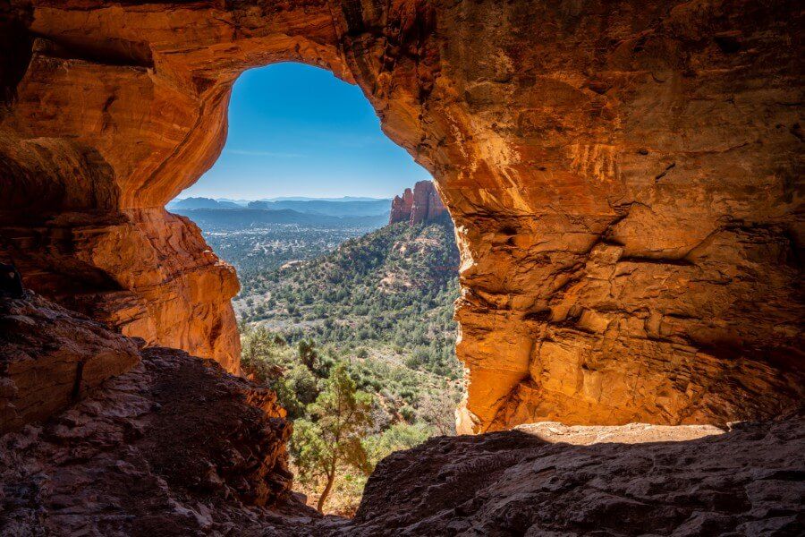 Cavernous chamber filled with orange glowing light and view over Sedona from Keyhole Caves